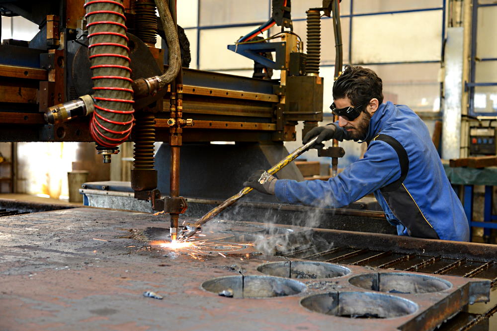 Ein Arbeiter schweisst in einer Fabrik ein Metallstück. Er trägt eine Schutzbrille.