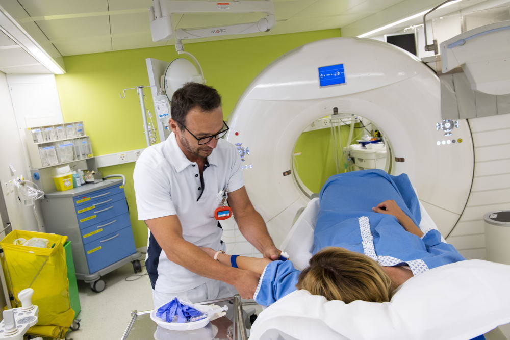 Ein Mann kümmert sich vor einer MRI-Untersuchung um eine Frau, die auf einer Trage liegt.