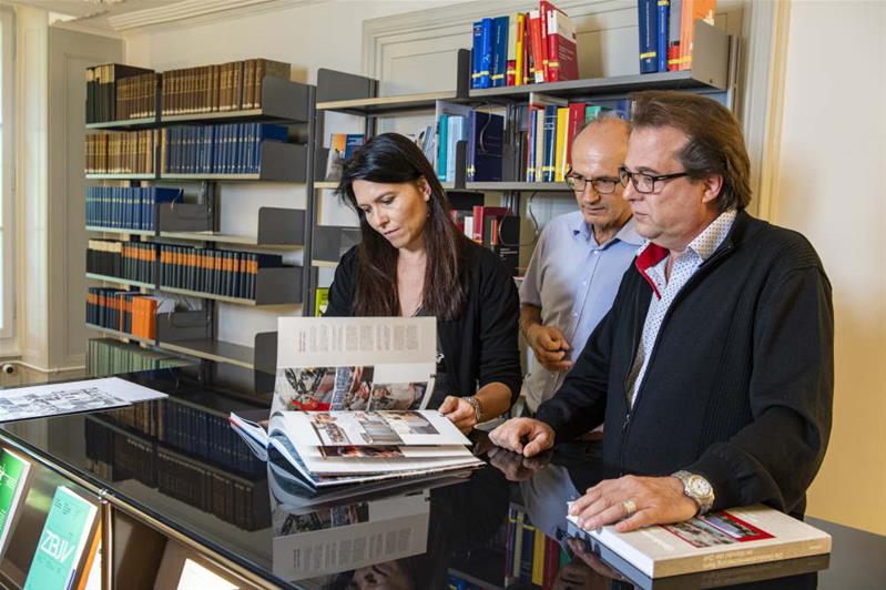 Eine Frau und zwei Männer schauen ein aufgeschlagenes Buch an.