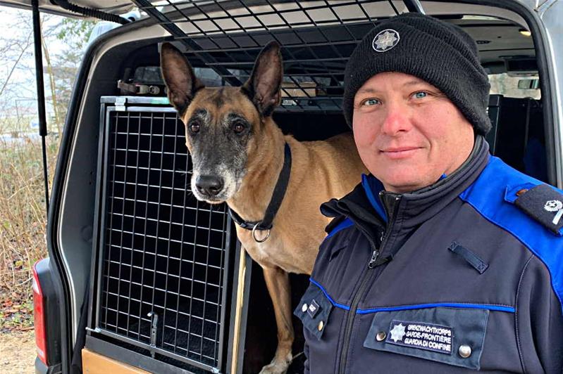 Ein Mann in Uniform des Bundesamts für Zoll- und Grenzschutz steht neben Dynamo, einem Diensthund.