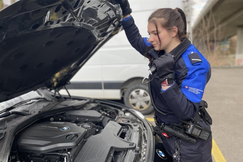 Eine junge Frau in einer Uniform des Bundesamts für Zoll und Grenzsicherheit hält an einem Grenzübergang ein Fahrzeug an.