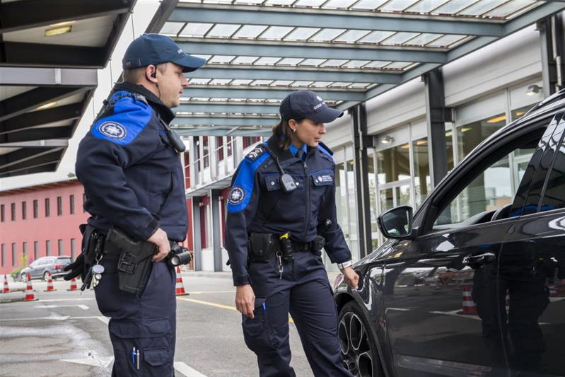 Eine Fachspezialistin und ein Fachspezialist für Zoll und Grenzsicherheit halten ein Fahrzeug an einem Grenzposten an.