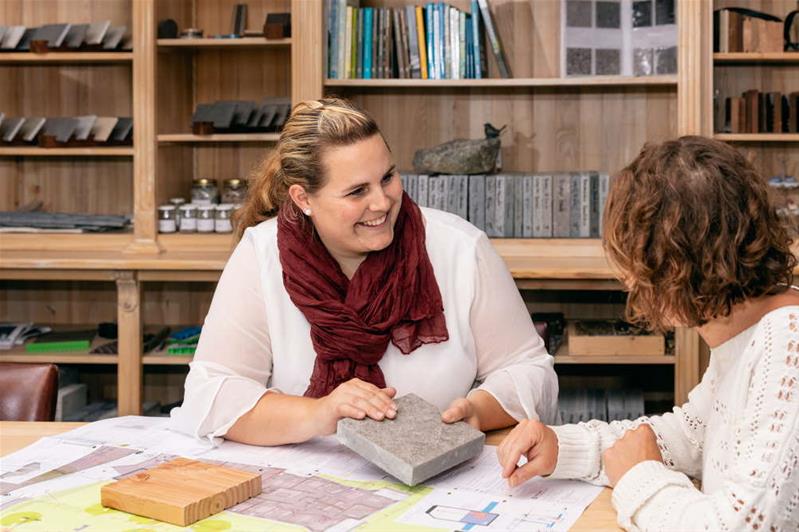 Eine Frau berät eine Kundin bei der Wahl des Bodenbelags für einen Aussensitzplatz.