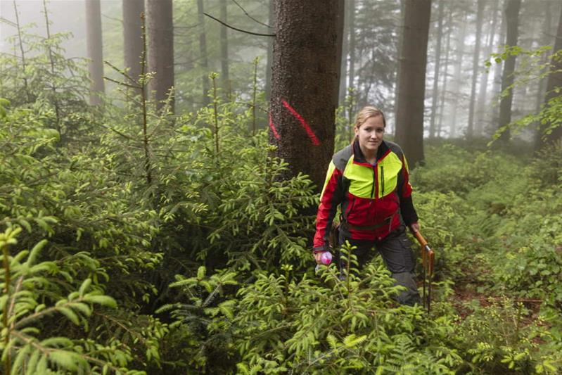 Eine junge Frau in Försterkleidung geht durch den Wald.