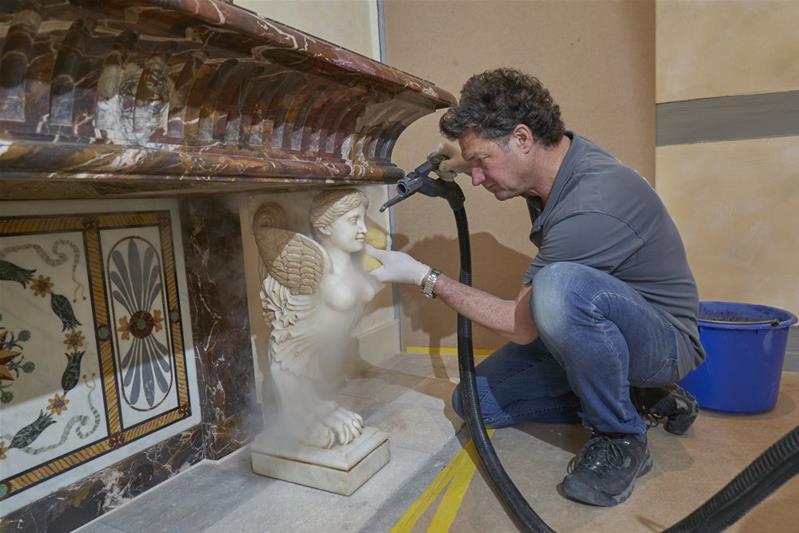 Thobias Hotz reinigt die Oberfläche einer Steinskulptur mithilfe einer Luftdruckpistole.