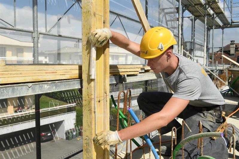 Ein Lernender nimmt Mass um eine Mauer aus Ziegeln zu bauen.