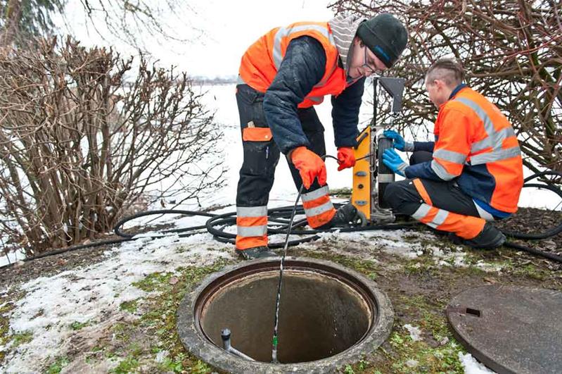 Zwei Lernende kontrollieren eine Wasserleitung unter der Strasse.