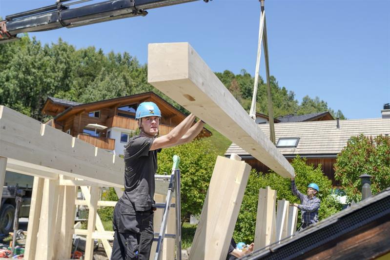 Ein Lernender bewegt auf einer Baustelle einen Balken mit einem Kran.