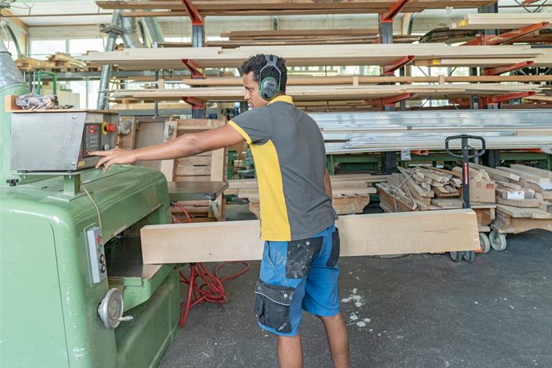 Ein Lernender schneidet ein Stück Holz mit einer Maschine.