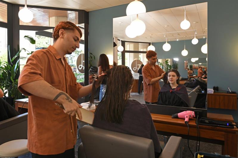 Ein Lernender bürstet die Haare einer Kundin.