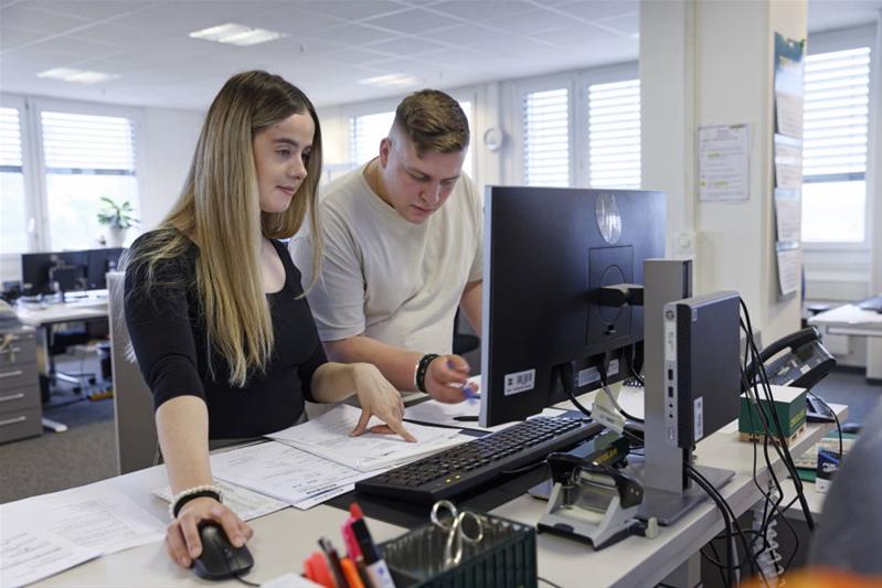 Eine Lernende und ihr Chef arbeiten im Büro vor einem Computer.