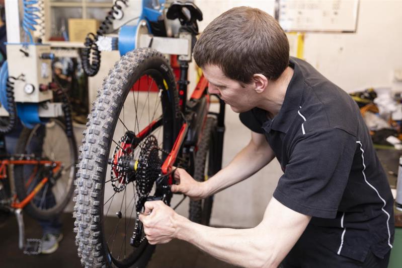 Ein Mechaniker arbeitet am Schaltwerk des Hinterrads eines Fahrrads.
