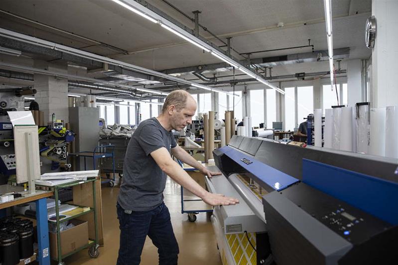 Ein Mann steht vor einer Druckmaschine in einer Druckerei.