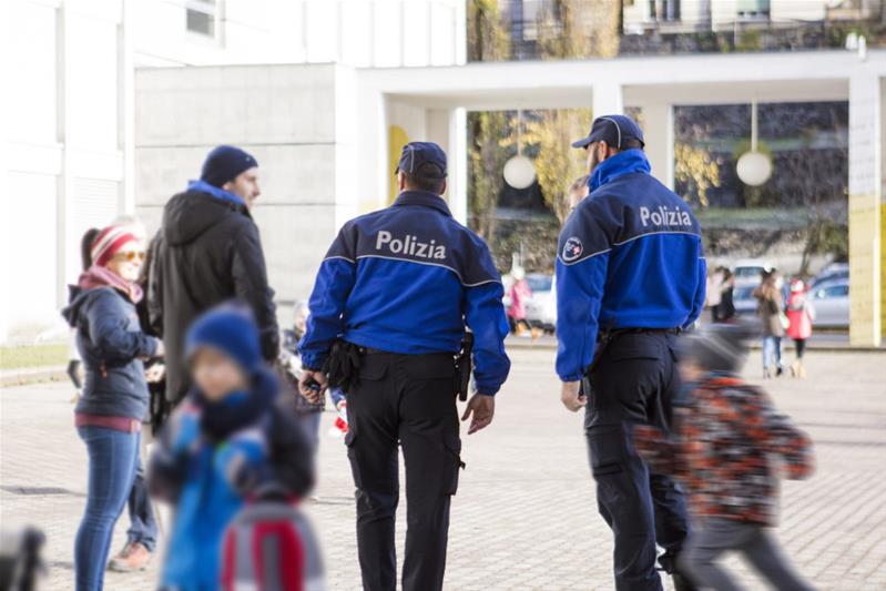 Zwei Polizisten sprechen mit Eltern auf einem Schulhof.