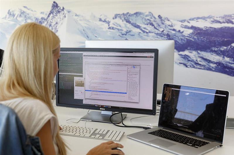 Eine junge Frau an zwei Bildschirmen in einem Büro.