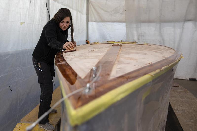 Eine junge Frau schleift den Rumpf eines Holzbootes.