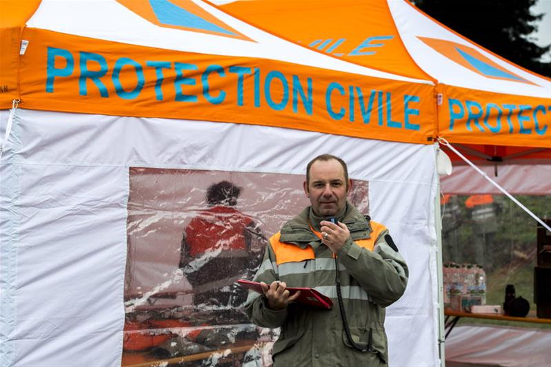 Ein Mann mit einem Funkgerät in der Hand steht vor einem Zelt des Zivilschutzes.
