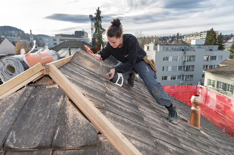 Eine Lernende verlegt Ziegel auf einem Dach.