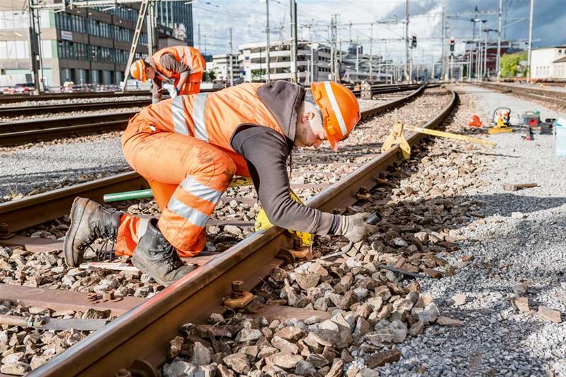 Ein Lernender arbeitet draussen am Boden und kontrolliert ein Gleis.