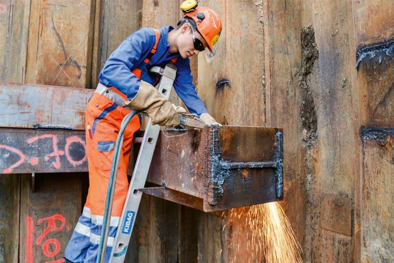 Ein Lernender schneidet und schweisst Metall auf einer Baustelle.