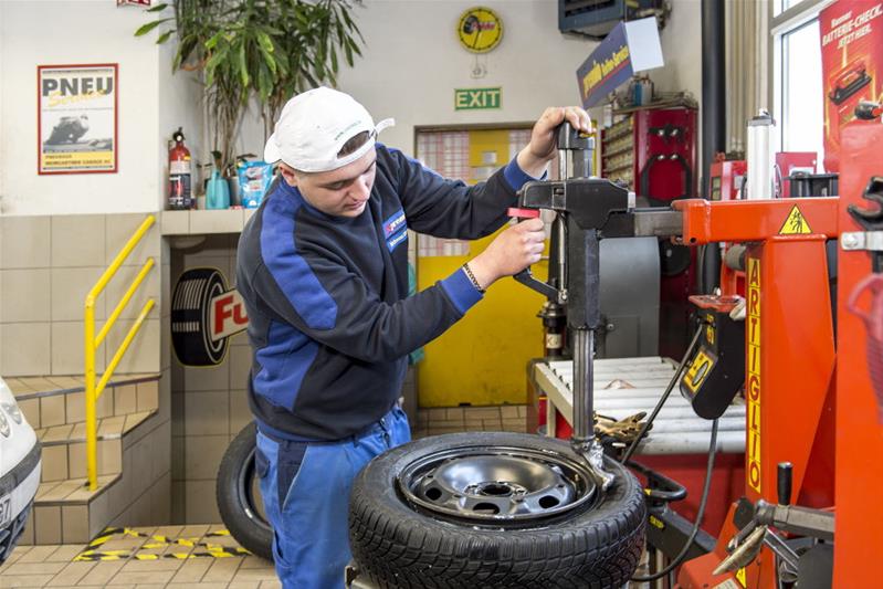 Ein Lernender arbeitet mit einem Gerät an einem Autoreifen.