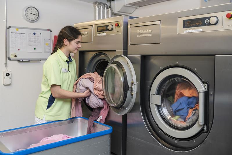 Eine Lernende lädt Wäsche in eine Waschmaschine.