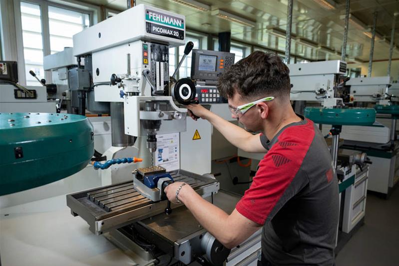 Ein Lernender bohrt mithilfe einer Maschine Löcher in ein Metallstück.
